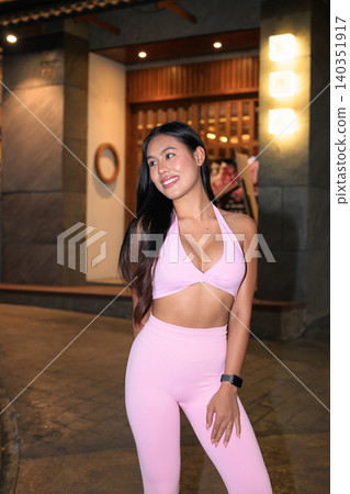 Smiling Asian woman in pink activewear looking away on night street Smiling Asian woman in pink activewear looking away on night street 140351917