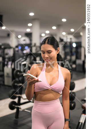 Happy Asian woman in pink sportswear checking smartphone in gym Happy Asian woman in pink sportswear checking smartphone in gym 140351932