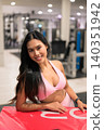 Happy Asian woman in pink sportswear leaning on red plyo box in gym 140351942
