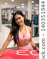 Smiling Asian woman in pink activewear leaning on red plyo box in gym 140351944