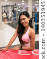 Cheerful Asian woman in pink activewear leaning on red plyo box in gym 140351945