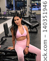 Confident Asian woman in pink activewear sitting on gym bench 140351946