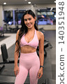 Smiling Asian woman in pink activewear posing in modern gym 140351948