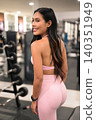 Smiling Asian woman in pink sportswear posing from behind in gym 140351949