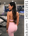 Smiling Asian woman in pink fitness clothes posing from behind in gym 140351951