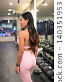 Asian woman in pink fitness apparel looking away by dumbbell rack in gym 140351953