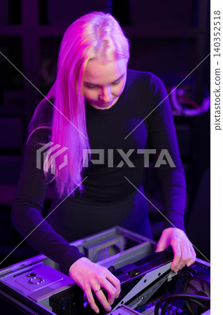 Young woman upgrading a gaming PC under purple lighting, assembling hardware components with focus Young woman upgrading a gaming PC under purple lighting, assembling hardware components with focus 140352518