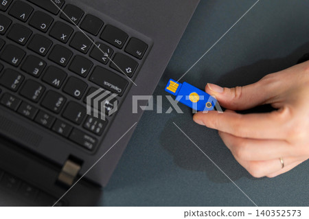 Adult woman uses blue USB security key beside a laptop in a tech office workspace Adult woman uses blue USB security key beside a laptop in a tech office workspace 140352573