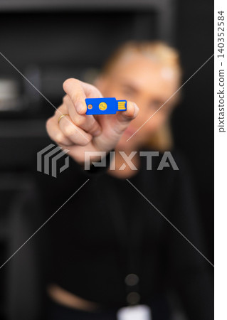 Female IT security technician in her 30s holds a blue USB flash drive in a modern office setting Female IT security technician in her 30s holds a blue USB flash drive in a modern office setting 140352584