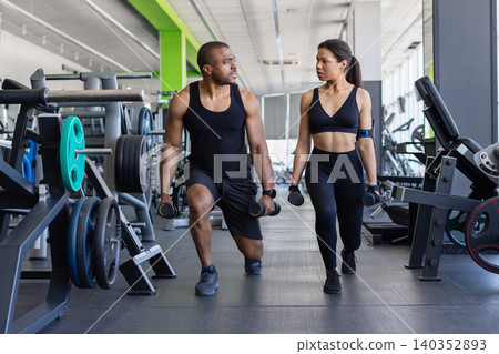 Young black fitness performing walking lunges with dumbbells in modern gym Young black fitness performing walking lunges with dumbbells in modern gym 140352893