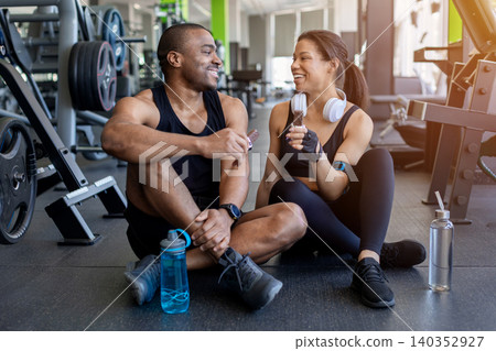Black enjoying protein snack bars after workout while sitting in gym Black enjoying protein snack bars after workout while sitting in gym 140352927