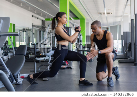 Personal trainer supervising young woman during lunge exercise in fitness center 140352966