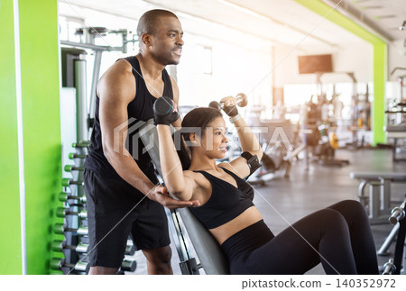 Personal trainer supervising young woman performing incline dumbbell shoulder press at gym Personal trainer supervising young woman performing incline dumbbell shoulder press at gym 140352972