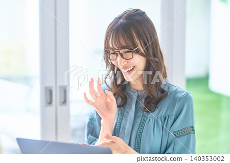 A woman wearing glasses smiles and waves at her laptop. A woman wearing glasses smiles and waves at her laptop. 140353002