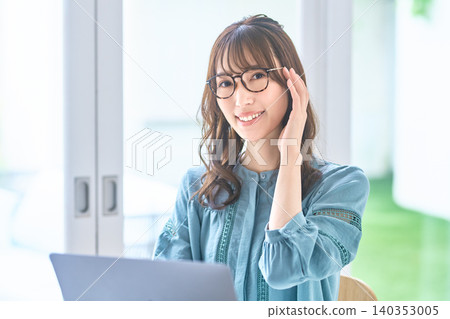 A woman smiles while adjusting her glasses in front of her computer. A woman smiles while adjusting her glasses in front of her computer. 140353005