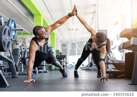 Black fitness giving high five while in push-up position on gym 140353028