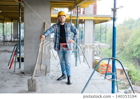 Construction worker standing with shovel at building site Construction worker standing with shovel at building site 140353194