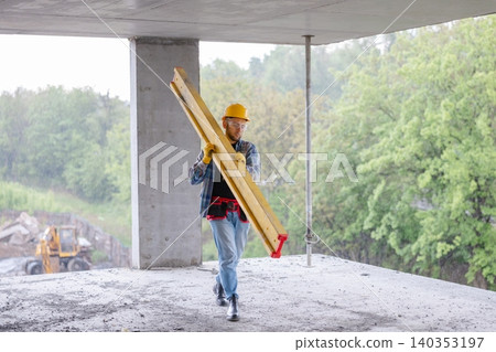 Construction worker carrying formwork beam on building site Construction worker carrying formwork beam on building site 140353197
