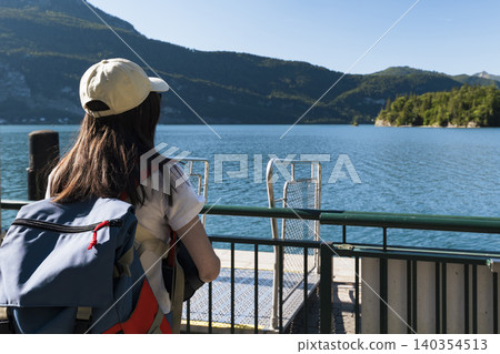 Young woman looking at the lake and mountains from a pier at Wolfgangsee in the Austrian Alps, expressing a connection with nature Young woman looking at the lake and mountains from a pier at Wolfgangsee in the Austrian Alps, expressing a connection with nature 140354513