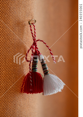 Two small red and white tassels hanging on a textured orange curtains Two small red and white tassels hanging on a textured orange curtains 140355001