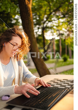 Woman working on laptop outdoors in park with setting sun Woman working on laptop outdoors in park with setting sun 140355046