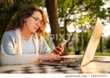 Woman working on laptop and smartphone outdoors in nature Woman working on laptop and smartphone outdoors in nature 140355077