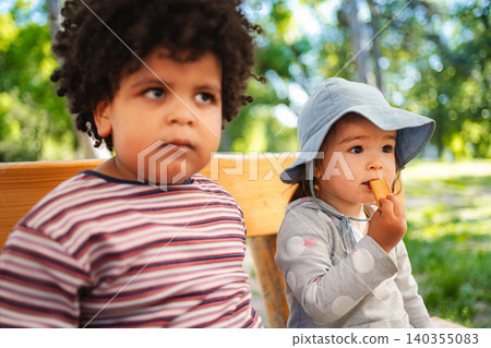 Diverse preschoolers snacking on a park bench outdoors 140355083