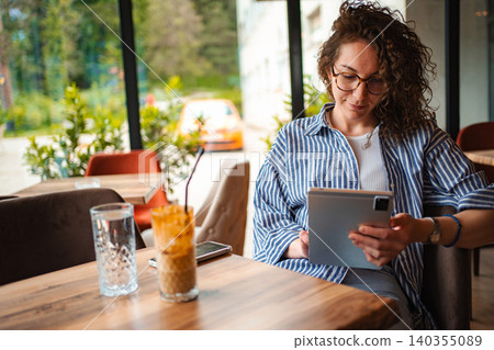 Woman working remotely using digital tablet in cafe Woman working remotely using digital tablet in cafe 140355089