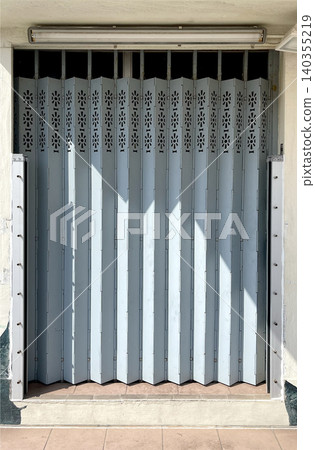 Accordion security gate with decorative cutouts and sunlight casting shadows Accordion security gate with decorative cutouts and sunlight casting shadows 140355219