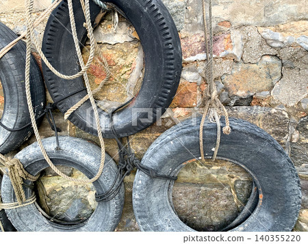 Old weathered tires and ropes hanging on a rustic stone wall Old weathered tires and ropes hanging on a rustic stone wall 140355220