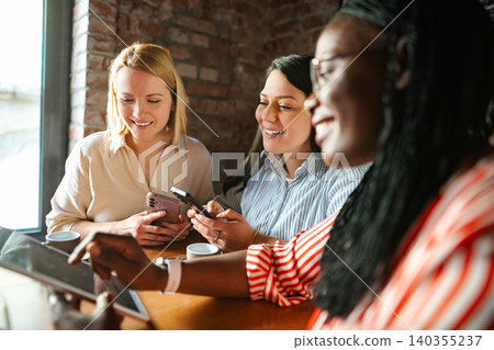 Diverse friends enjoying technology and smiling at cafe Diverse friends enjoying technology and smiling at cafe 140355237