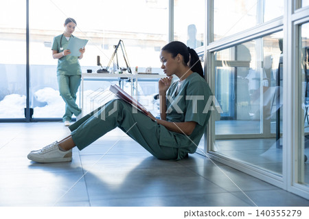 Dark-haired female doctor sitting on the floor and scrutinizing a medical history of the patient 140355279