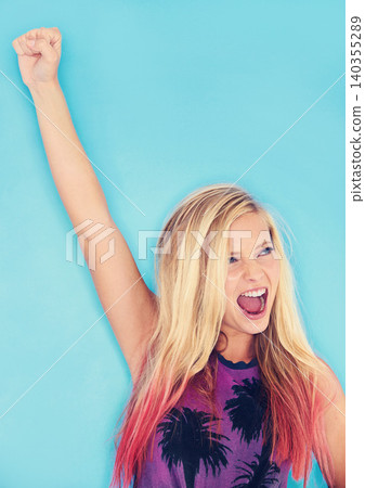 Woman, celebration and fist in studio for success, lottery winner and deal on blue background. Female person, energy and promo or yes for giveaway achievement, bonus and discount or prize and sale 140355289