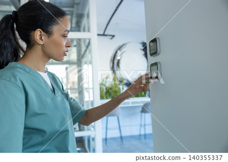 Long-haired woman in a lab coat standing near temperature panel and touching it Long-haired woman in a lab coat standing near temperature panel and touching it 140355337