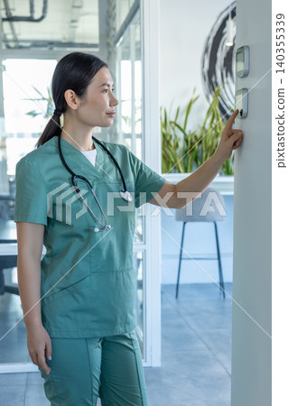 Long-haired woman in a lab coat standing near temperature panel and touching it Long-haired woman in a lab coat standing near temperature panel and touching it 140355339