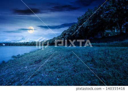 longest linden alley in europe on the Uzh river embankment at night. full moon over lime trees in summer. travel destination of transcarpathia. uzhhorod street cityscape beauty. mysterious fantasy longest linden alley in europe on the Uzh river embankment at night. full moon over lime trees in summer. travel destination of transcarpathia. uzhhorod street cityscape beauty. mysterious fantasy 140355416