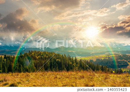 sunset over mountain landscape in september. green nature of carpathian mountains with coniferous forest. view of a scenery with rolling hills under cloudy sky. pasture near woods under with rainbow sunset over mountain landscape in september. green nature of carpathian mountains with coniferous forest. view of a scenery with rolling hills under cloudy sky. pasture near woods under with rainbow 140355423