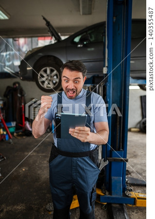 Excited mechanic celebrating success with digital tablet in auto repair shop Excited mechanic celebrating success with digital tablet in auto repair shop 140355487