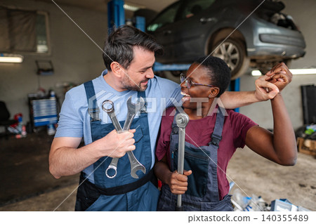 Two happy mechanics holding wrenches and celebrating success in auto repair shop Two happy mechanics holding wrenches and celebrating success in auto repair shop 140355489