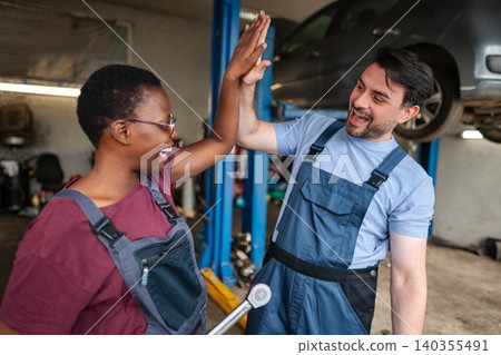 Two happy mechanics giving high five after repairing car in auto repair shop Two happy mechanics giving high five after repairing car in auto repair shop 140355491