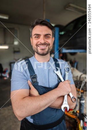Portrait of a smiling mechanic holding wrenches in a garage Portrait of a smiling mechanic holding wrenches in a garage 140355494