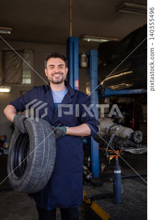 Mechanic holding a tire in a garage, smiling at the camera Mechanic holding a tire in a garage, smiling at the camera 140355496