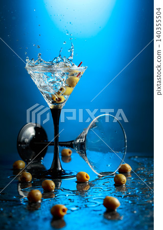 Green olives and glass of martini on a black stone table. Green olives and glass of martini on a black stone table. 140355504