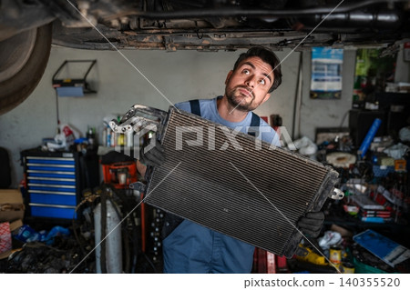 Mechanic holding car radiator and looking up at vehicle in garage 140355520