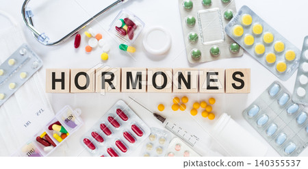 HORMONES. Word on wooden blocks on the table. Medical concept with pills, vitamins, stethoscope and syringe in the background. HORMONES. Word on wooden blocks on the table. Medical concept with pills, vitamins, stethoscope and syringe in the background. 140355537