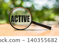 Magnifying glass with text ACTIVE on wooden table and green background. 140355682