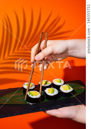 Aesthetic shot of wooden chopsticks taking a roll from a line on bright orange backdrop Aesthetic shot of wooden chopsticks taking a roll from a line on bright orange backdrop 140355751