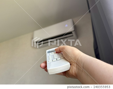 Close-up female hand holding white remote control pointing at air conditioner, bright modern apartment interior, climate control and home comfort concept Close-up female hand holding white remote control pointing at air conditioner, bright modern apartment interior, climate control and home comfort concept 140355953