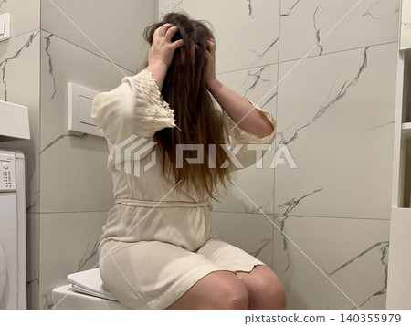Woman in bathrobe sitting on bathroom with face in hands, messy hair, emotional burnout and psychological crisis concept Woman in bathrobe sitting on bathroom with face in hands, messy hair, emotional burnout and psychological crisis concept 140355979