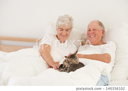 Senior couple, bed and cat for smile, embrace and love in morning for bonding and cuddle. Mature man, woman and kitty pet, happy and retirement to enjoy marriage and old people in bedroom at home 140356102